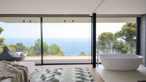 A modern bathroom with a large bathtub, a glass shower enclosure, and a view of the sea. - Villa Falguerines - Six Bedroom Villa, Sleeps 12 (Begur)