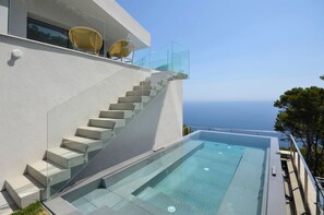 Un bâtiment moderne doté d’un escalier en verre menant à une piscine à débordement située sur le toit, d’où l’on peut admirer la vue sur la mer.