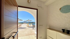 Una habitación con vista a una zona de piscina, una puerta de madera, una pared blanca con textura y una lámpara en el techo.
