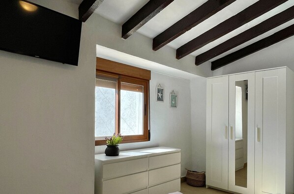 Una habitación con ventana, un aparador blanco, un armario y un televisor montado en la pared.