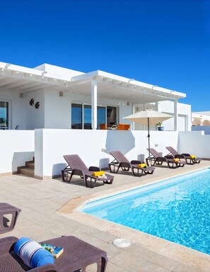 A modern poolside area with lounge chairs and a covered seating area.