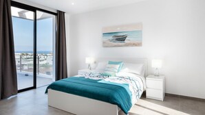 A modern bedroom with a large bed, a view of the sea through a sliding glass door, and a painting of a boat on the wall. - Villa Bernialiss - Three Bedroom Villa, Sleeps 6 (Puerto del Carmen)