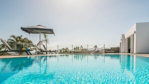 A clear blue pool with lounge chairs and umbrellas, surrounded by palm trees and a modern building. - Villa Canwell - Four Bedroom Villa, Sleeps 8 (Puerto del Carmen)