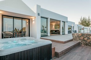 Ein modernes Haus mit Whirlpool, Sitzgelegenheit im Freien und einer Steinmauer.