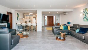 A modern living room with a sofa, two coffee tables, and a TV. There is a kitchen area with bar stools and a dining table. - Villa Canwell - Four Bedroom Villa, Sleeps 8 (Puerto del Carmen)