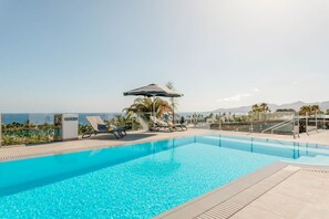 A clear blue pool with lounge chairs and umbrellas, surrounded by palm trees and a view of the ocean. - Villa Canwell - Four Bedroom Villa, Sleeps 8 (Puerto del Carmen)