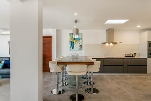 A modern kitchen with a dining area, featuring a wooden table and white chairs, a stainless steel range hood, and a large abstract painting on the wall. - Villa Canwell - Four Bedroom Villa, Sleeps 8 (Puerto del Carmen)