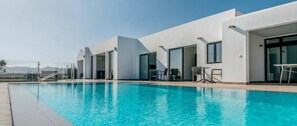 A modern hotel with a swimming pool, outdoor seating, and a view of the mountains.