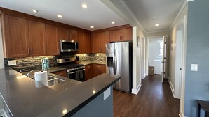 Une cuisine moderne avec des meubles en bois, des appareils électroménagers en acier inoxydable, un plan de travail en marbre et des spots encastrés au plafond.