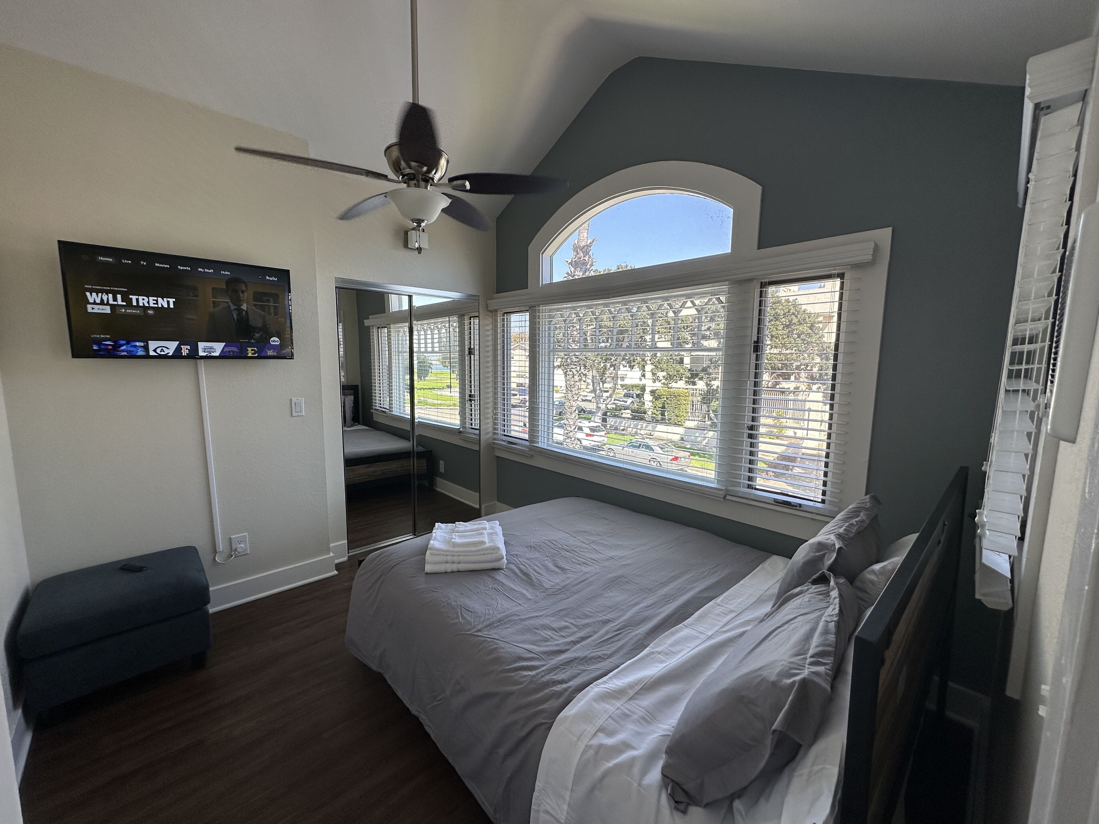 Une chambre à coucher avec un lit, un ventilateur de plafond, une télévision et de grandes fenêtres.