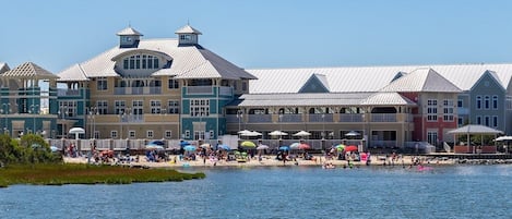 A waterfront hotel with multiple buildings, a beach area with umbrellas, and a view of the water.