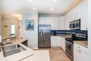 A modern kitchen with white cabinets, stainless steel appliances, and a blue tiled backsplash. - Sunset Island 2 Hidden Cove Way, Unit 4A (Ocean City)