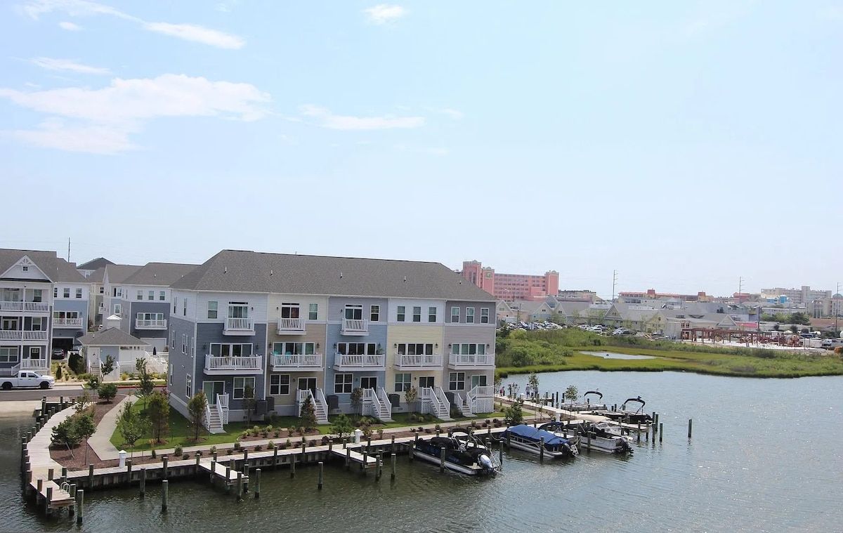 A waterfront residential building with multiple balconies, a dock with boats, and a marina in the background.