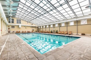 An indoor swimming pool with a tiled floor, a glass ceiling, and wooden lounge chairs around the pool. - Sunset Island 2 Hidden Cove Way, Unit 4A (Ocean City)