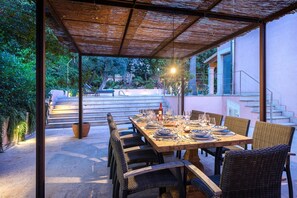 Ein Essbereich im Freien mit überdachter Terrasse, einem gedeckten Tisch und einer Treppe zu einem Gebäude.