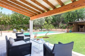 Une terrasse extérieure avec des meubles en osier, une table en verre et une piscine en arrière-plan.