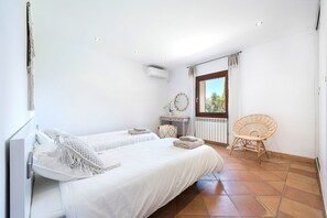 Ein Schlafzimmer mit zwei Betten, einem Sessel, einem Fenster mit Vorhängen und einer Heizung.