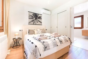Ein Schlafzimmer mit einem Bett, einem Nachttisch mit Lampe, einer Wand-Klimaanlage und einer Tür zu einem anderen Raum.