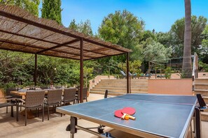 Un espace de jeu de ping-pong en plein air, comprenant un filet, des chaises et une table.