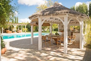 Un área de comedor al aire libre techada, con una piscina al fondo.