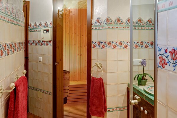 Une salle de bain avec des murs carrelés, une porte en bois, un porte-serviettes, un lavabo agrémenté d’une plante verte et un espace douche.