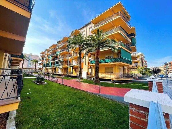 Un hôtel à plusieurs étages doté de balcons, d’une pelouse verdoyante et d’un chemin rouge.