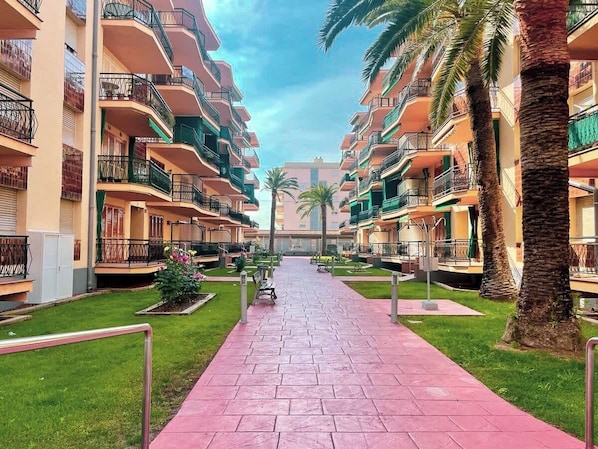 Un couloir d’hôtel avec des balcons, des palmiers et une allée pavée.