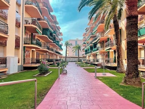 A hotel corridor with balconies, palm trees, and a paved walkway.