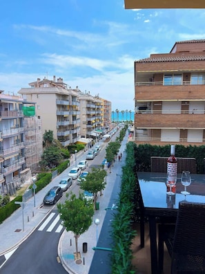 Un immeuble résidentiel à plusieurs étages doté de balcons, une rue avec des voitures et un trottoir pour les piétons.