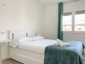 Une chambre avec un lit simple, une tête de lit blanche, une couvre-lit turquoise et une fenêtre avec des rideaux verts.