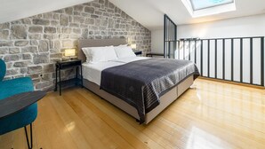 Une chambre avec un mur en pierre, une lucarne, un lit, une table de chevet et une chaise.