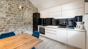 Une cuisine moderne avec des meubles blancs, un mur en pierre et une table à manger en bois.