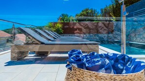 Un espace aménagé au bord de la piscine, avec des chaises longues, un mur en pierre et une vue dégagée sur la mer.