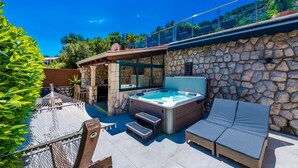 Un bain à remous avec un mur en pierre en arrière-plan, des sièges d’extérieur et une pergola.