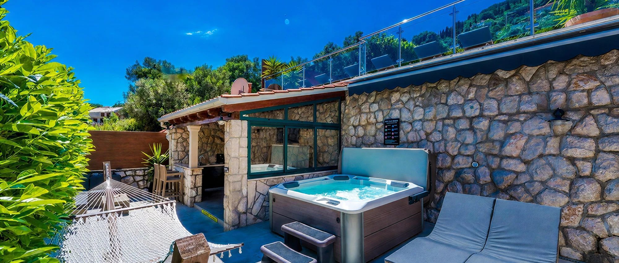 A hot tub with steps, a lounge chair, and a stone wall.