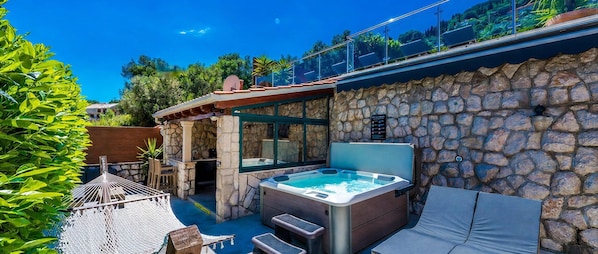 A hot tub with steps, a lounge chair, and a stone wall.