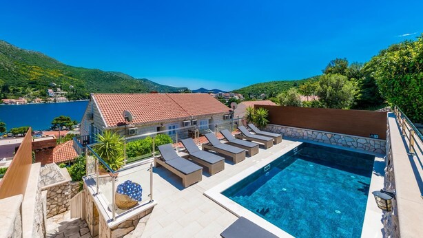 Un espace aménagé au bord de la piscine, avec des chaises longues, une piscine en pierre et une vue sur un lac et des collines.