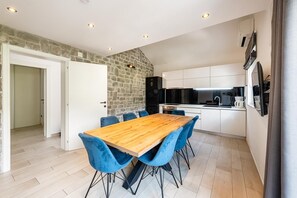 A modern kitchen with white cabinets, a black refrigerator, and a wooden dining table with blue chairs.