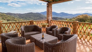 A covered outdoor seating area with wicker furniture and a view of mountains.