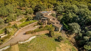 A stone house with a tiled roof, surrounded by lush greenery and hills.