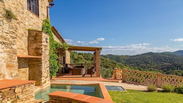 A stone building with a pool, outdoor seating, and a view of the mountains.
