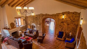 A rustic interior with stone walls, a fireplace, leather sofas, and wicker chairs.