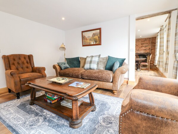 A living room with a brown leather armchair, a brown sofa with multiple cushions, a wooden coffee table with magazines, and a patterned rug.