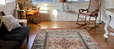 A room with a ceiling fan, a large rug, a rocking chair, a sofa, and a table.