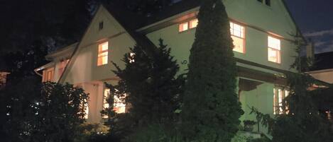 A two-story house with multiple windows, surrounded by greenery and trees.
