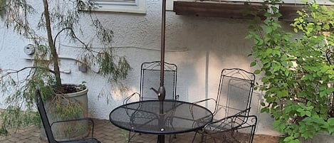 A patio area with a round table and four chairs, an umbrella, and potted plants.