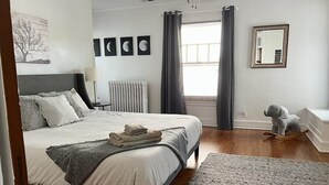 A bedroom with a large bed, a radiator, a window with curtains, a mirror, and a stuffed elephant toy. - Historic Oak Park Residence (Oak Park)