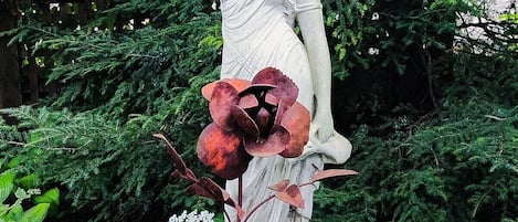 A statue of a woman holding a vase, surrounded by greenery and a wooden fence.