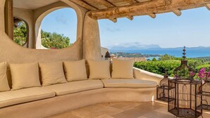 Un canapé beige aux lignes courbes, agrémenté de coussins, un plafond en bois et une vue sur la mer et les montagnes.