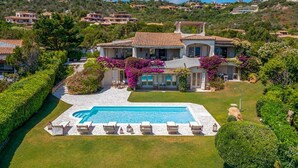 Une grande maison avec une piscine, entourée de pelouses et de haies bien entretenues.